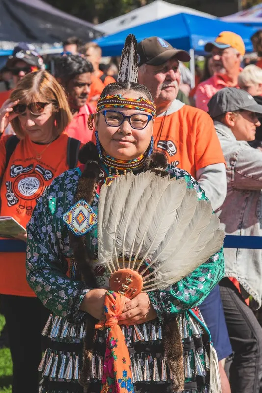 A person wearing elaborate regalia and glasses holding a large feathered fan