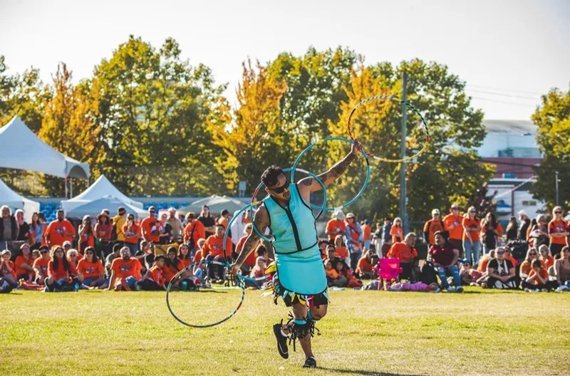 A hoop dancer performing with multiple yellow hoops in a sunlit field