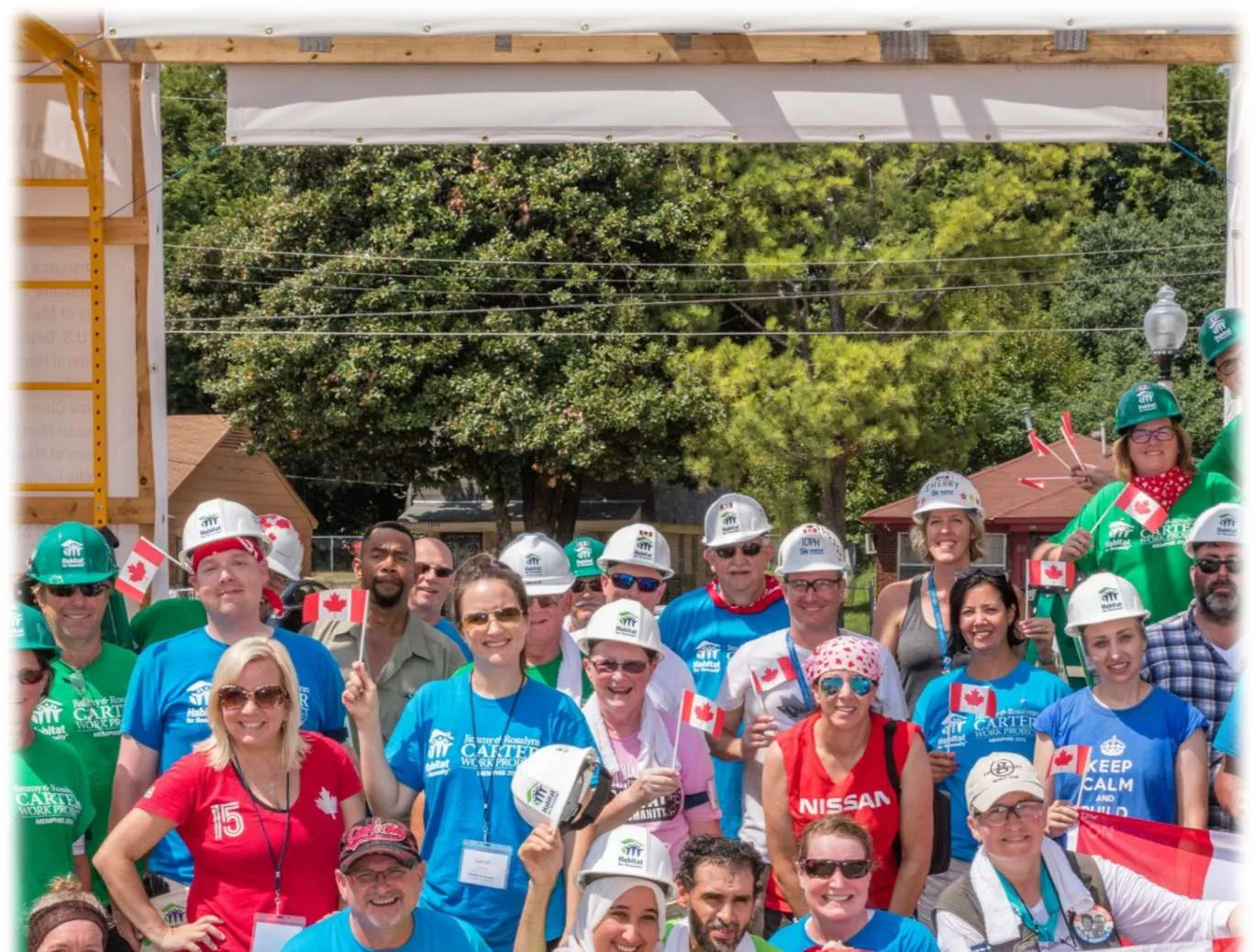 Top half of a large group of Habitat for Humanity volunteers and staff wearing hard hats and holding Canadian flags