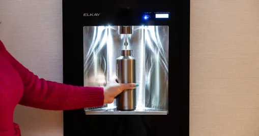 A person's hand holding a reusable metal bottle under a hotel water refill station