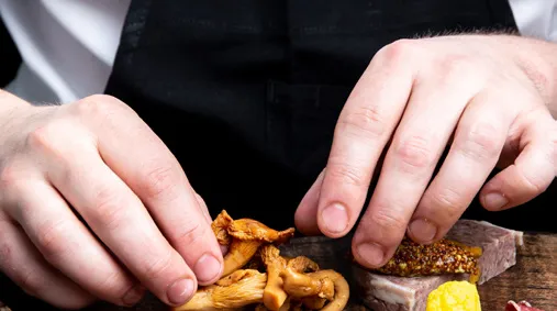 A chef's hands carefully placing mushrooms and garnishes on a gourmet platter