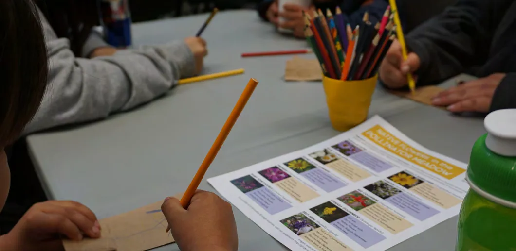 Close-up of a child drawing with colored pencils at a table.