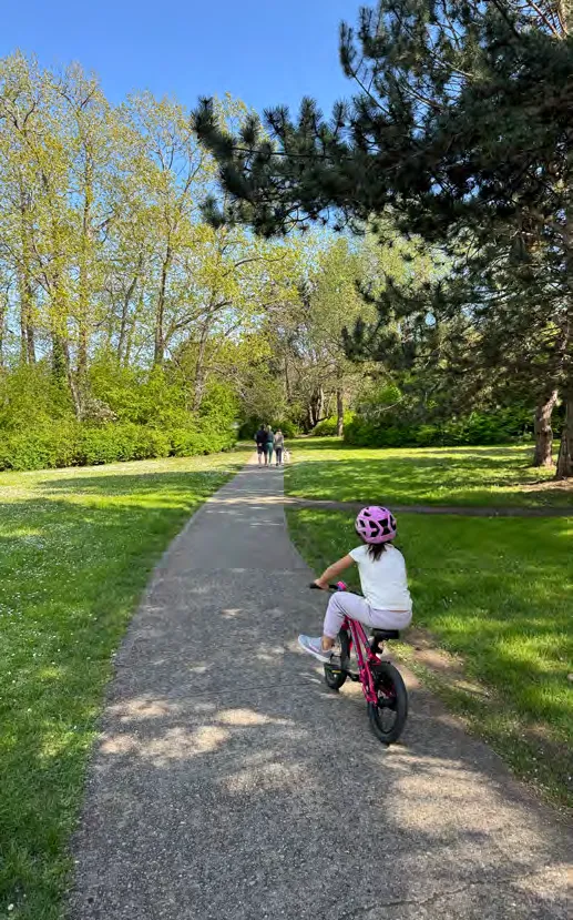 A child riding a bike on a paved path in a park.
