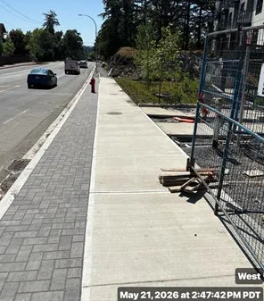 Street-level view of a new concrete sidewalk and paved curb area on Helmcken Road dated May 21, 2026