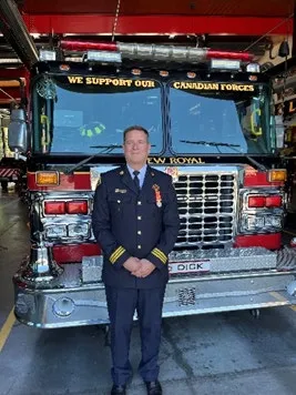 Assistant Chief Heath Bevan in dress uniform standing in front of a fire truck