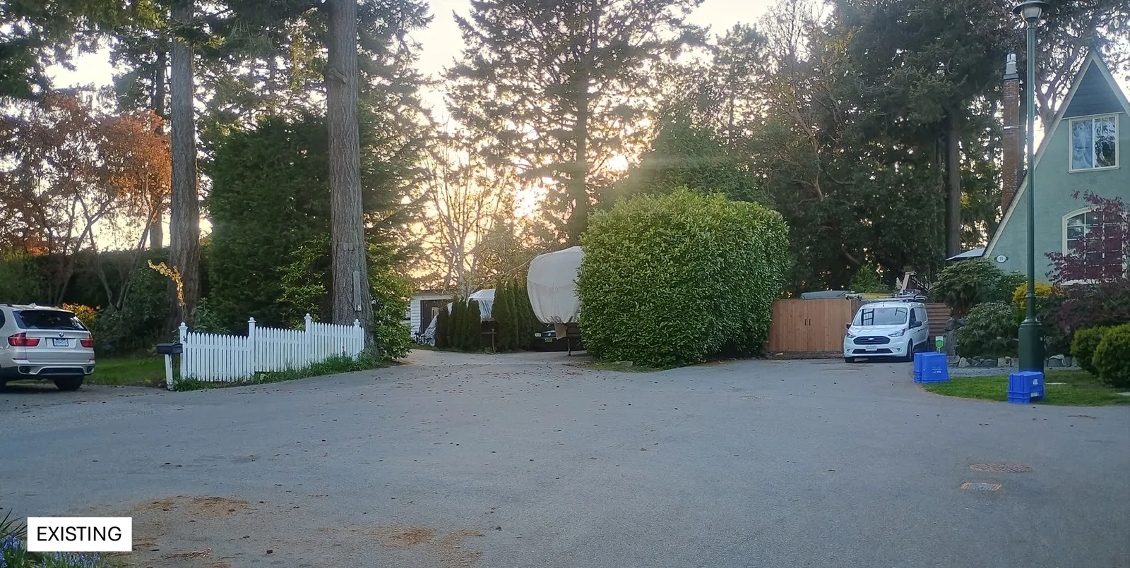 Photograph showing the existing street view of the property with a white fence, hedges, and trees