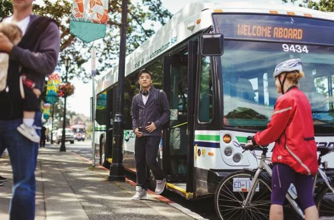 Passengers boarding a white BC Transit bus, including a cyclist with a bike
