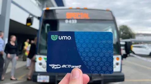 Hand holding a blue Umo transit payment card in front of a bus