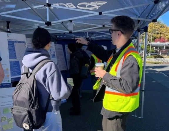 A BC Transit staff member in a high-visibility vest speaking with a member of the public at an engagement event