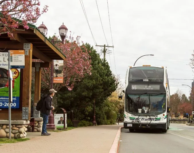 A double-decker BC Transit bus picking up a passenger at a suburban bus stop