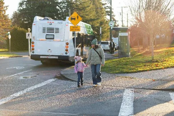 A woman and small child walking across a crosswalk away from a BC Transit bus
