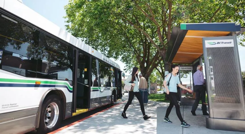 Passengers walking toward a bus waiting at a bus stop shelter with trees in the background
