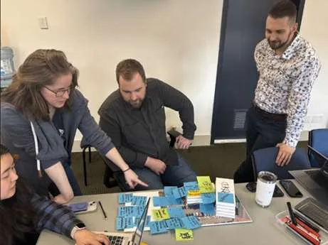 Photo of IPD team members gathered around a table with architectural plans and sticky notes during a planning session