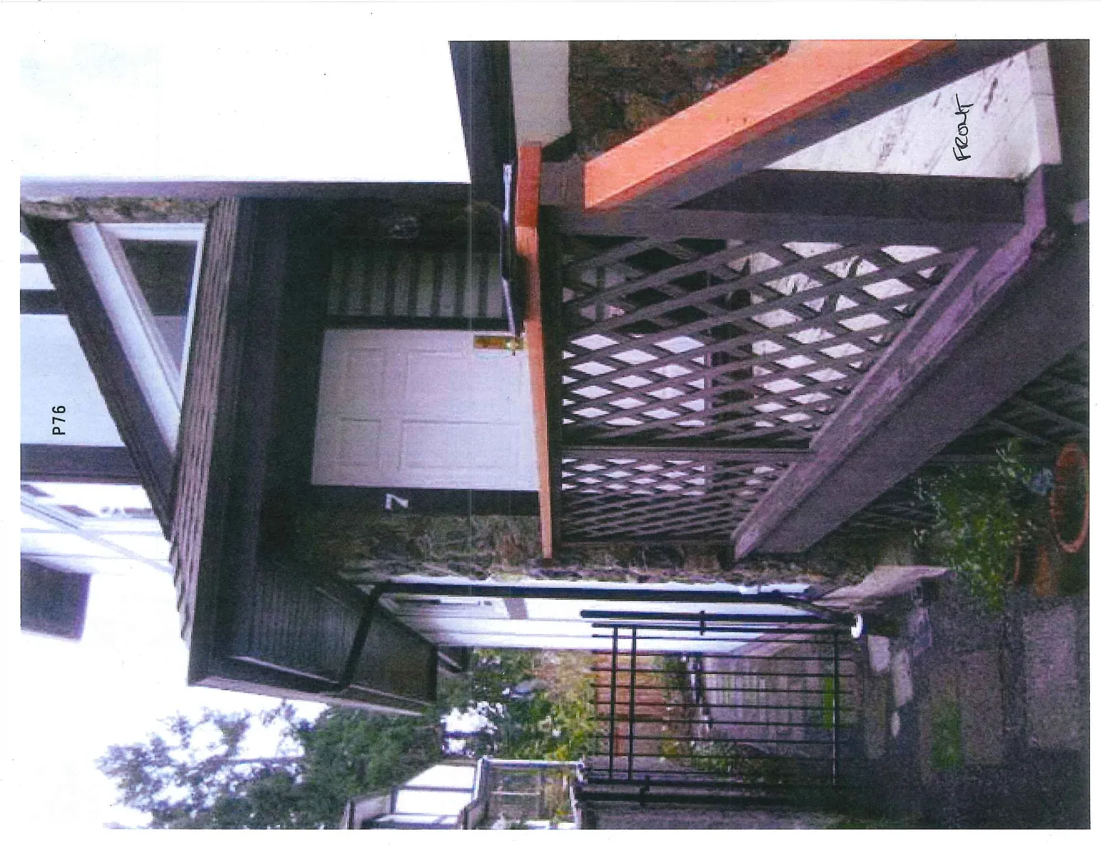 Side view of the front porch featuring dark-stained lattice railing and a black metal side gate