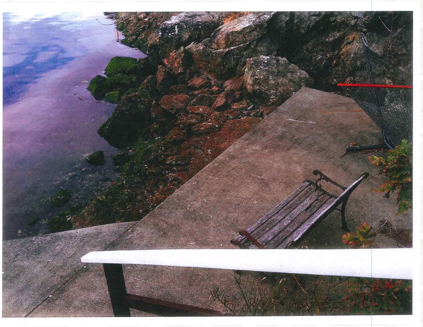 Concrete patio area with a wooden bench and a hammock located next to a rocky shoreline.