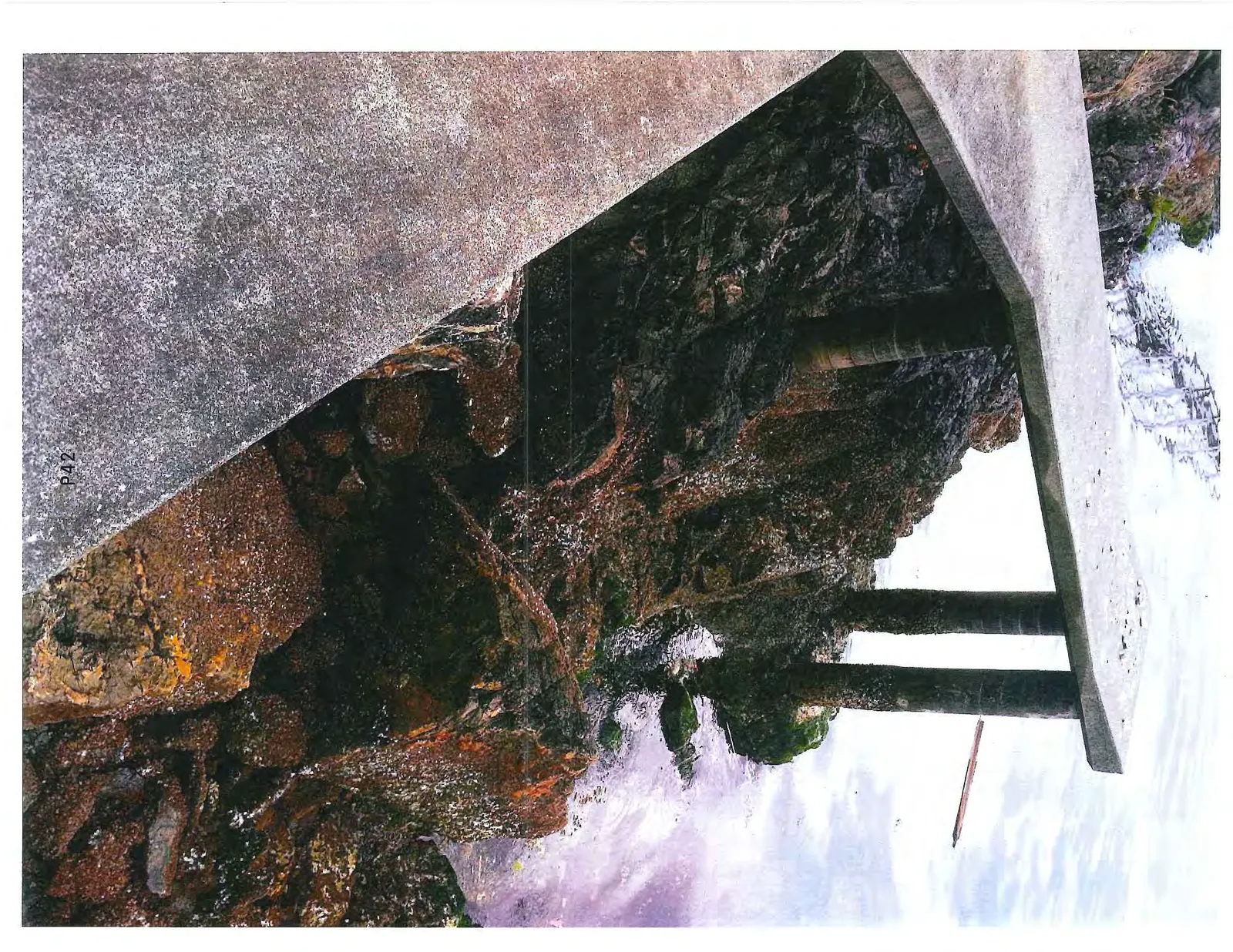 Underside of the concrete platform showing support pillars and the rocky shoreline.