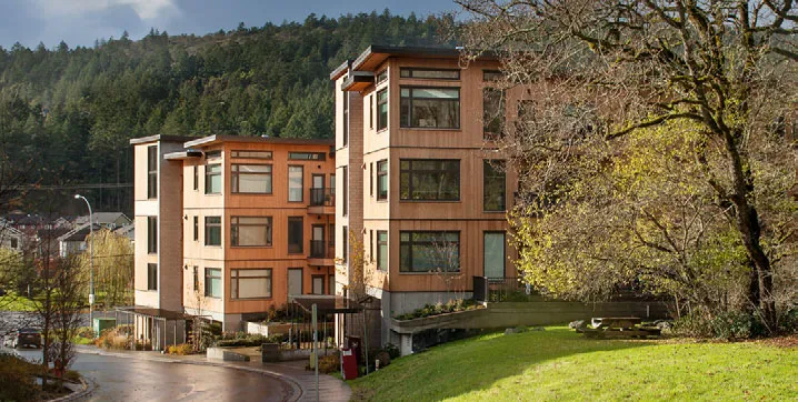 Modern multi-story residential buildings with wood-toned cladding integrated into a sloped, treed landscape