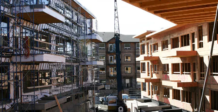 Multi-story residential building under construction with extensive scaffolding and visible framing