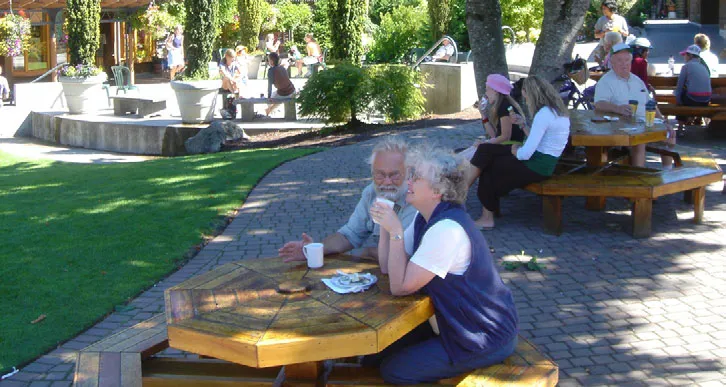 People relaxing and socializing at outdoor wooden picnic tables in a sunlit plaza