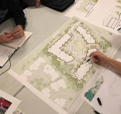 Circular-cropped photograph of individuals reviewing and pointing to a project site plan