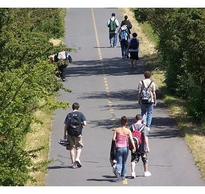 People walking and cycling on a paved trail lined with trees.