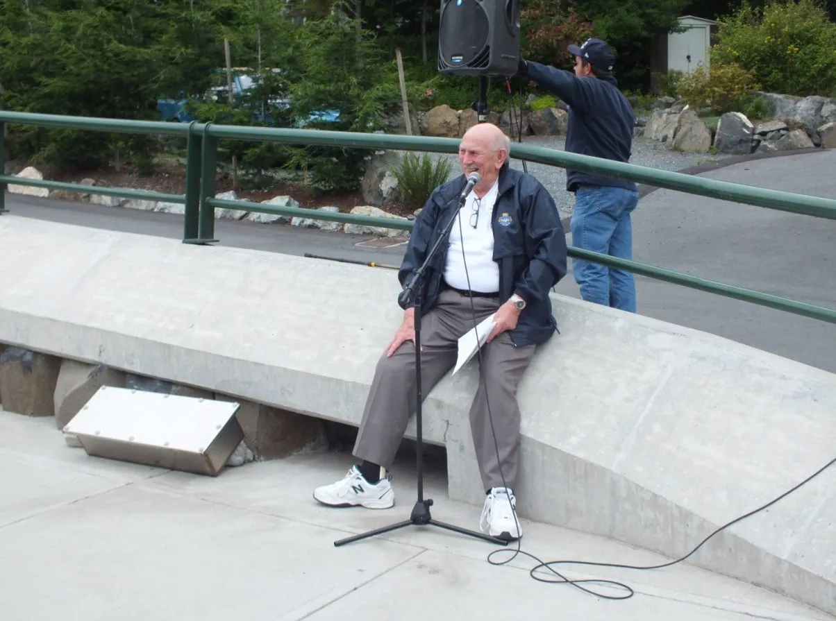 Mayor Hill sitting on a concrete wall speaking into a microphone at a ceremony.