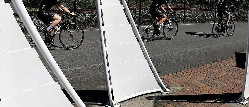 Three cyclists on a road passing by white structures