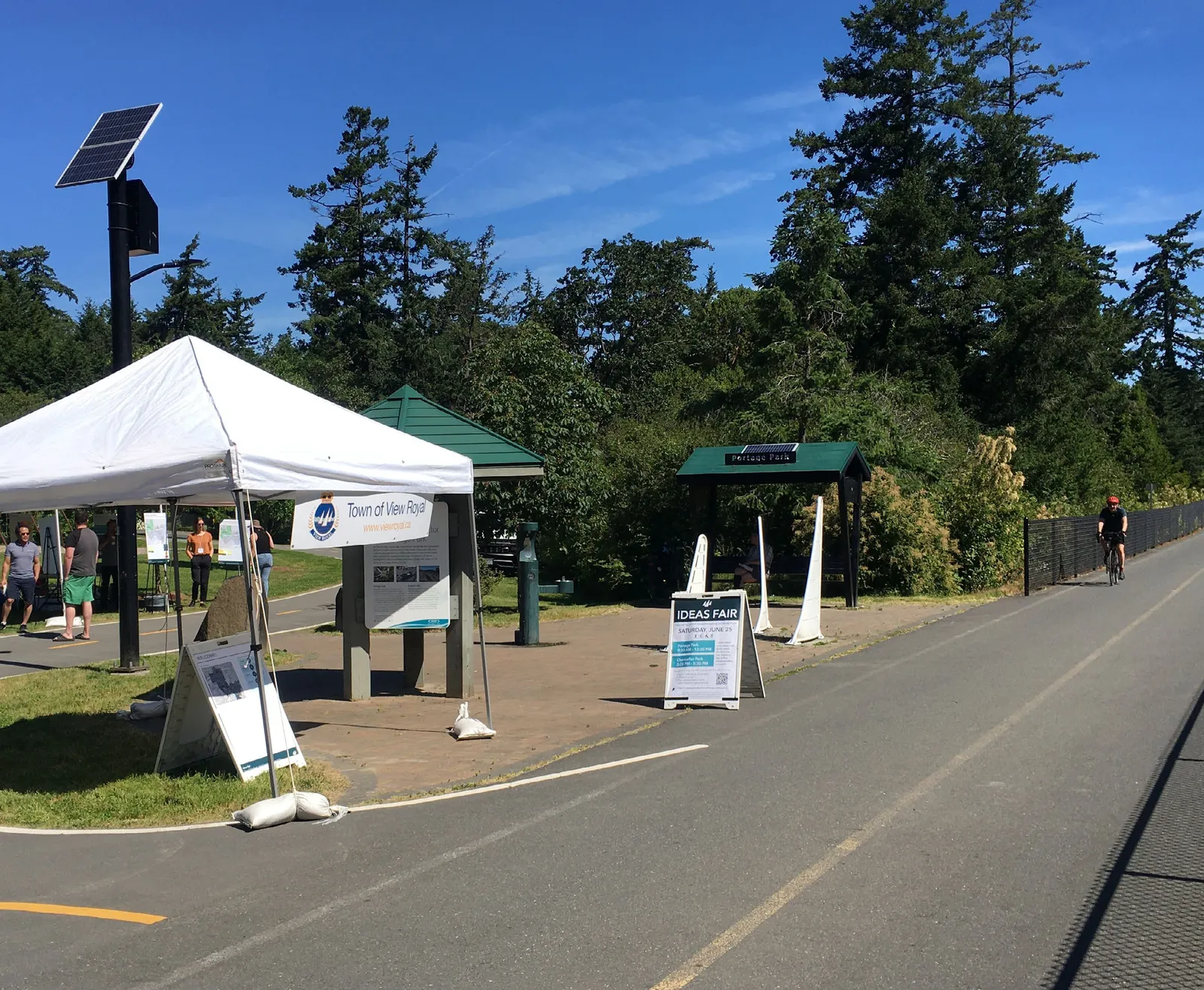 Photo of an "Ideas Fair" outdoor event at a park with informational tents and display boards situated next to a paved multi-use trail.