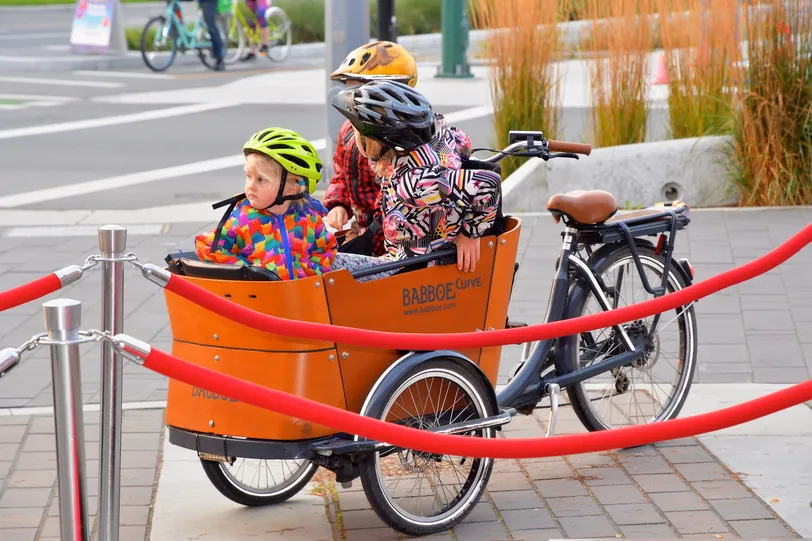 Children in the front box of an orange Babboe cargo bike