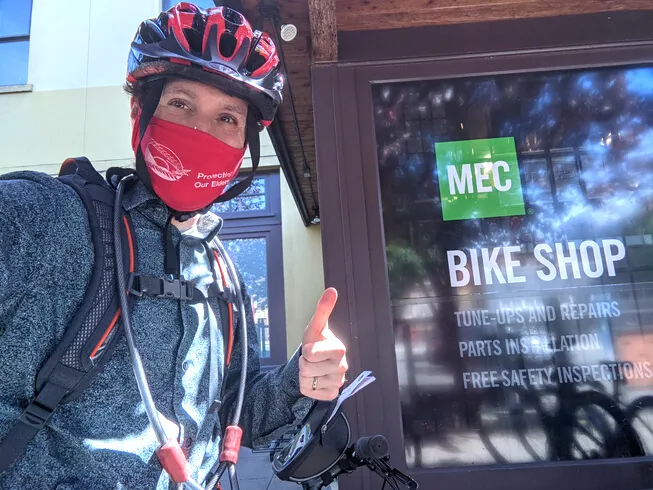 Man in cycling gear giving a thumbs up in front of MEC Bike Shop