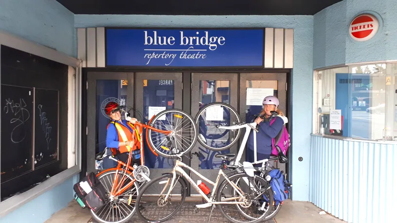 Two cyclists with bikes in front of Blue Bridge Repertory Theatre entrance