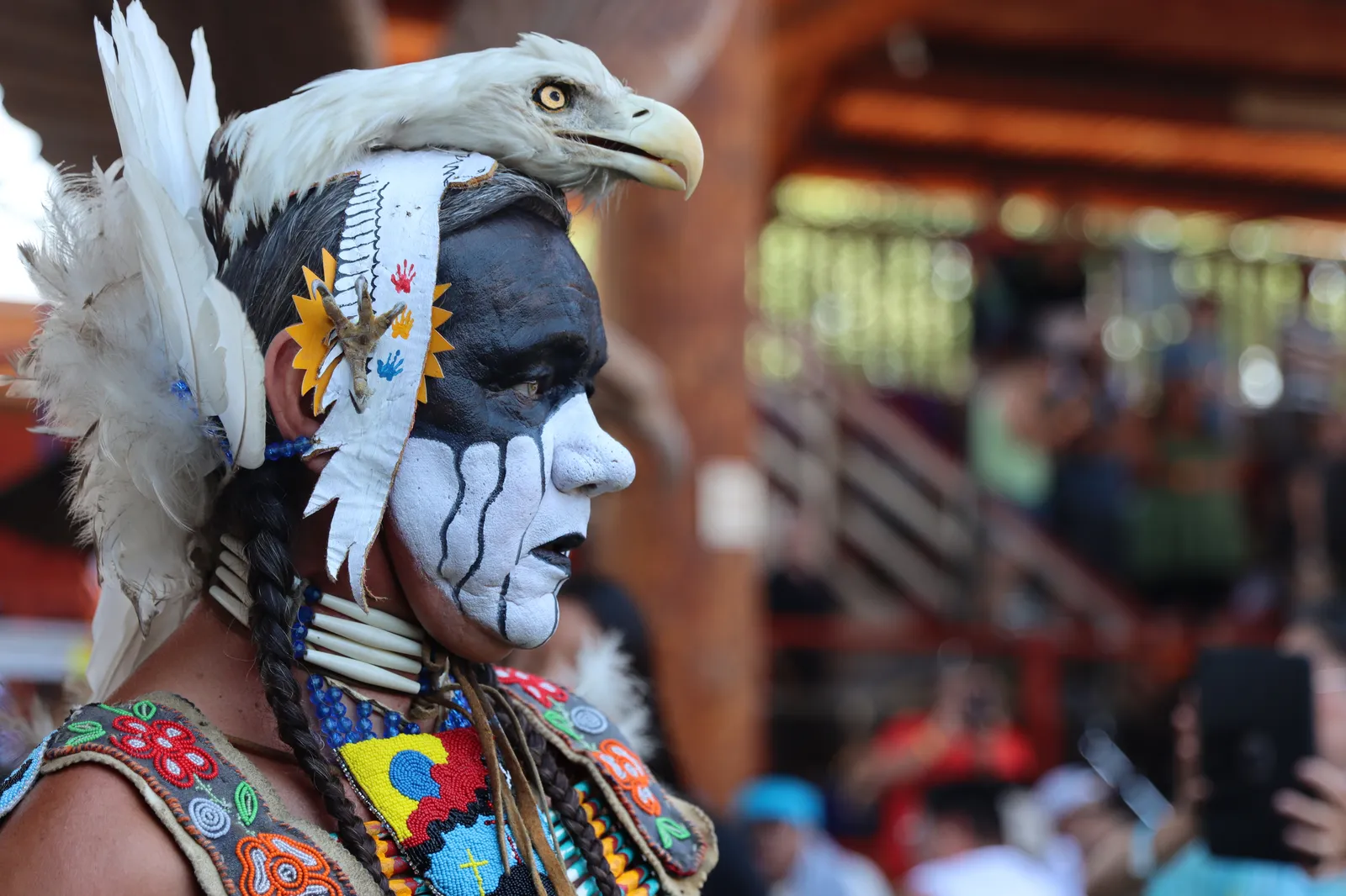 A person in traditional Indigenous regalia with face paint and an eagle headdress