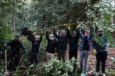A group of youth in a forest, some holding shovels and one pointing towards a cleared area
