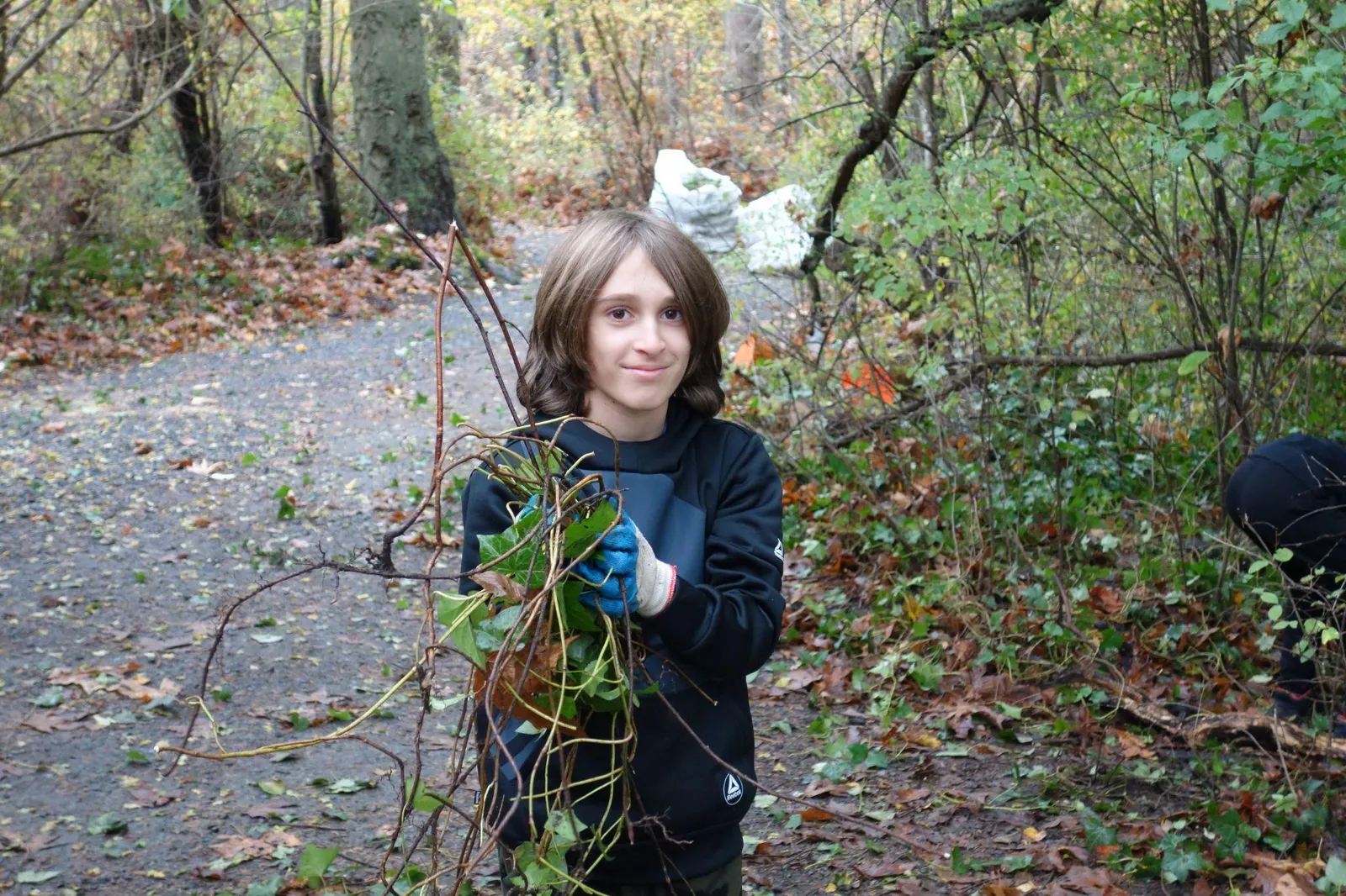 A young volunteer holding a bundle of pulled invasive vines in a park