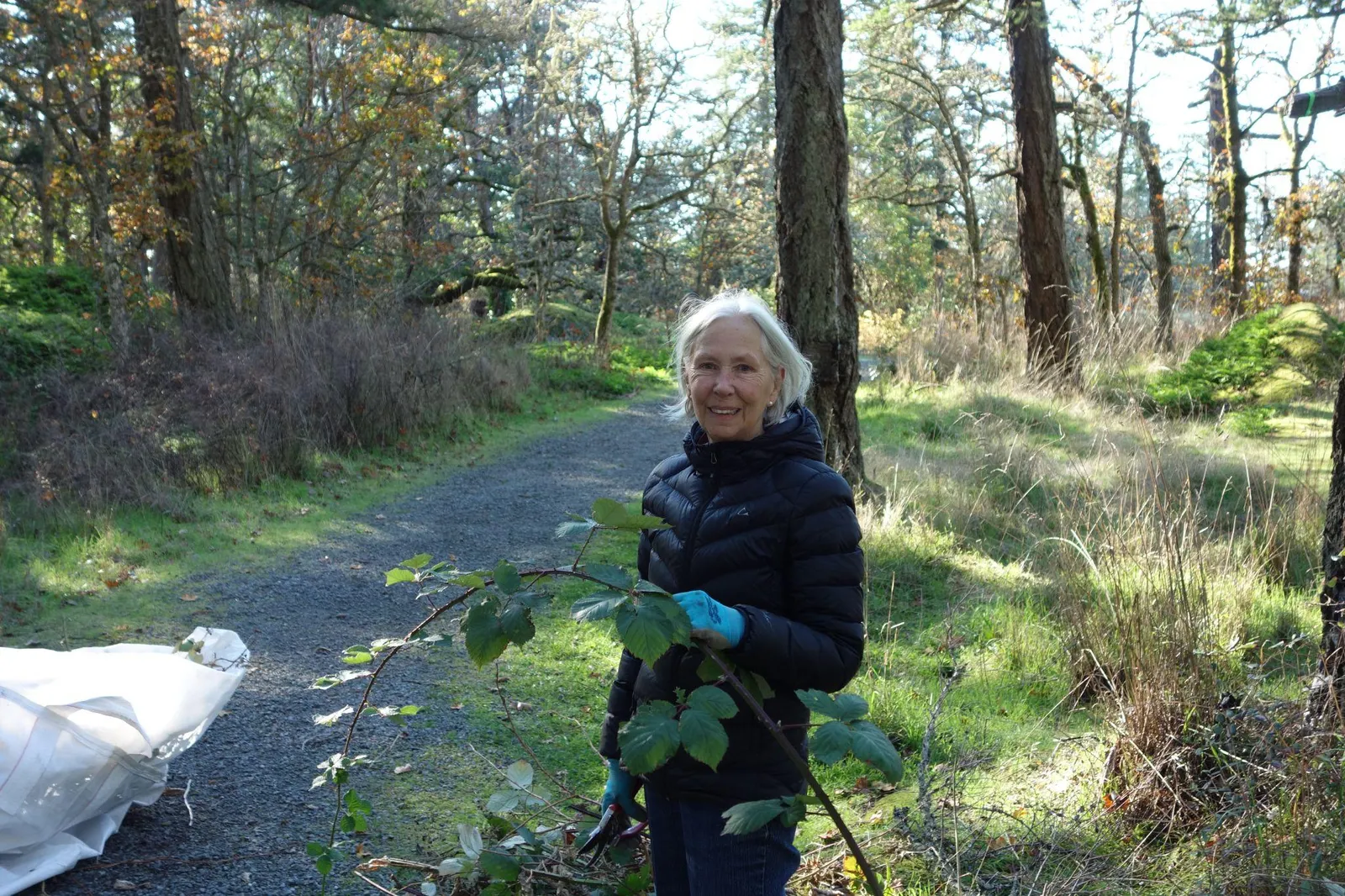 A woman smiling on a trail while holding a cut invasive plant