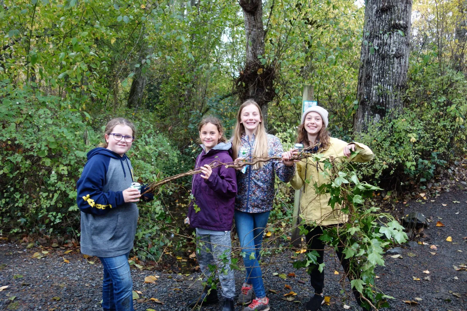 Four young students standing together and holding a long invasive vine they have removed