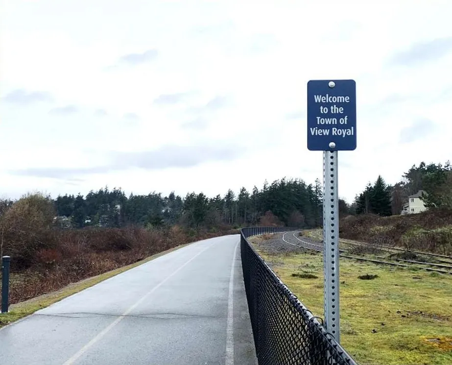 Photo of a paved pathway with a "Welcome to the Town of View Royal" sign next to a railway line