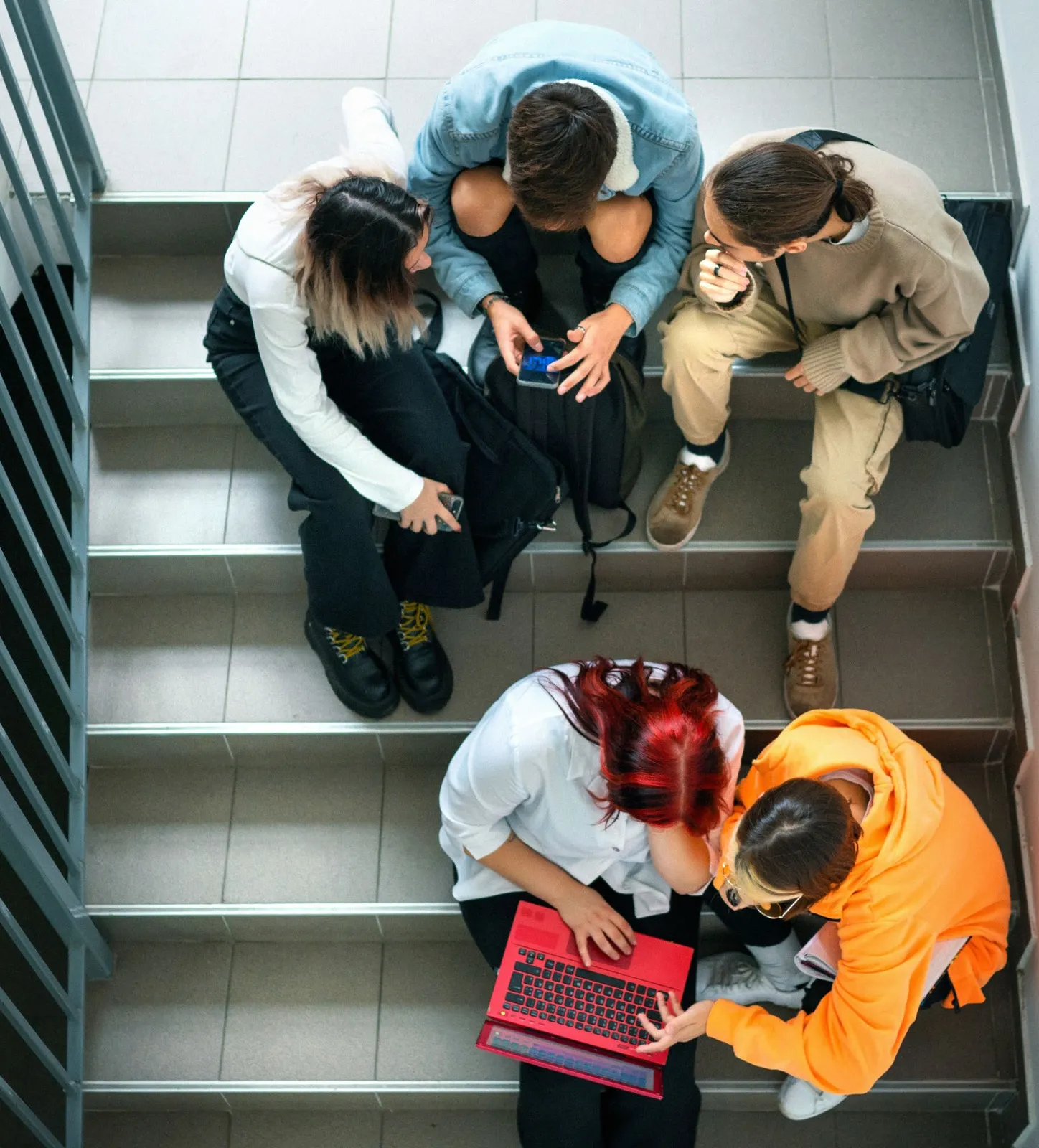 Four youth sitting on stairs using a phone and laptop