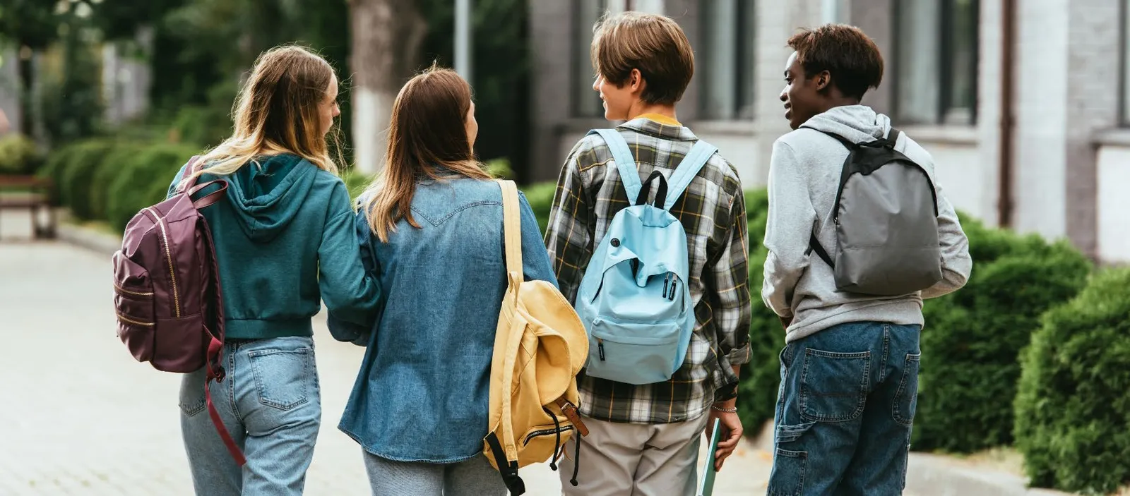 Four youth with backpacks walking together away from the camera