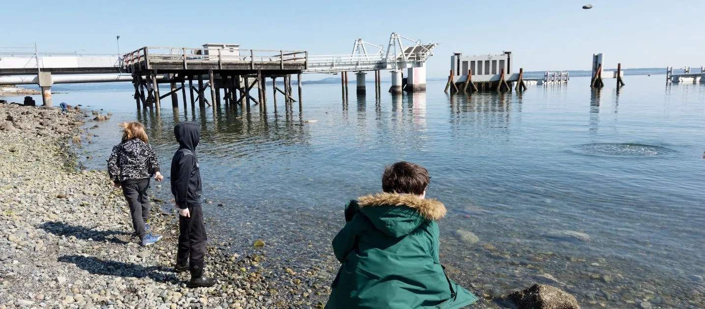 Three youth standing on a rocky beach by the ocean near a pier