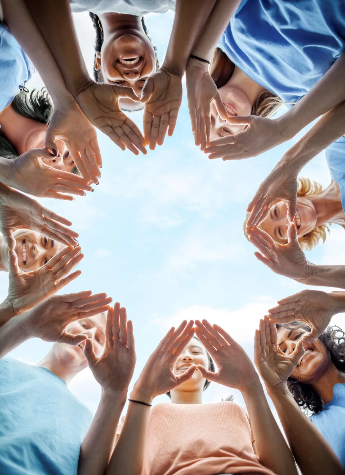 A circle of people seen from below, making heart shapes with their hands against the sky