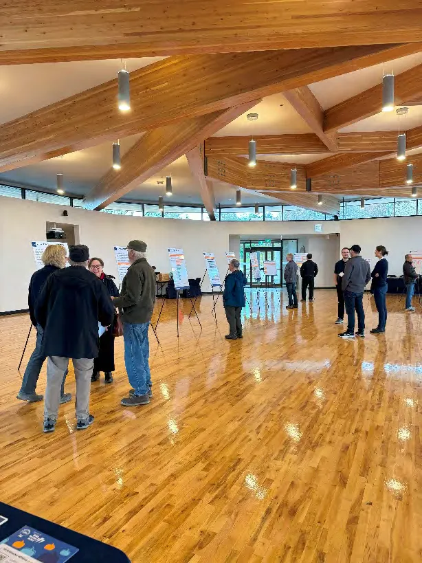Photo of a spacious room with high ceilings, where community members are gathered to view informational display boards.