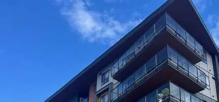The upper stories and roofline of a modern residential building featuring dark siding, wood accents, and glass-railed balconies