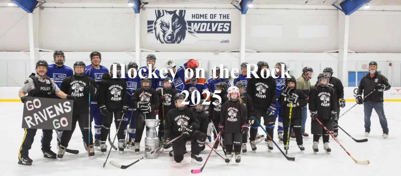 A group photo of dozens of hockey players in black and white "South Island Ravens" jerseys and blue "Wolves" jerseys posing on the ice with a trophy. Text reading "Hockey on the Rock 2025" is overlaid on the center, and a banner reading "HOME OF THE WOLVES" is in the background.