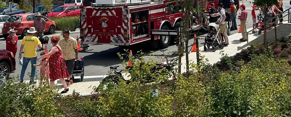 Base of fire truck with ladder extended and people gathered around at a community event