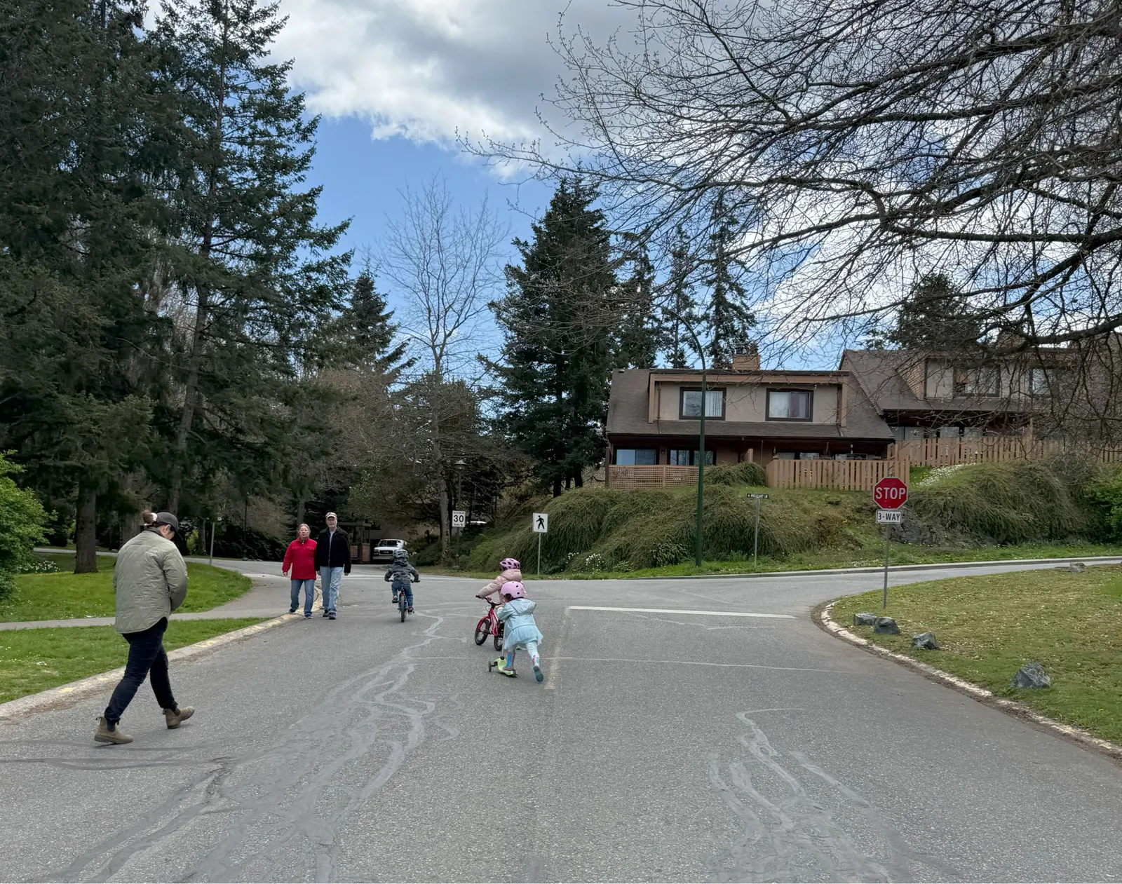 People walking and children on bikes and scooters at a residential intersection