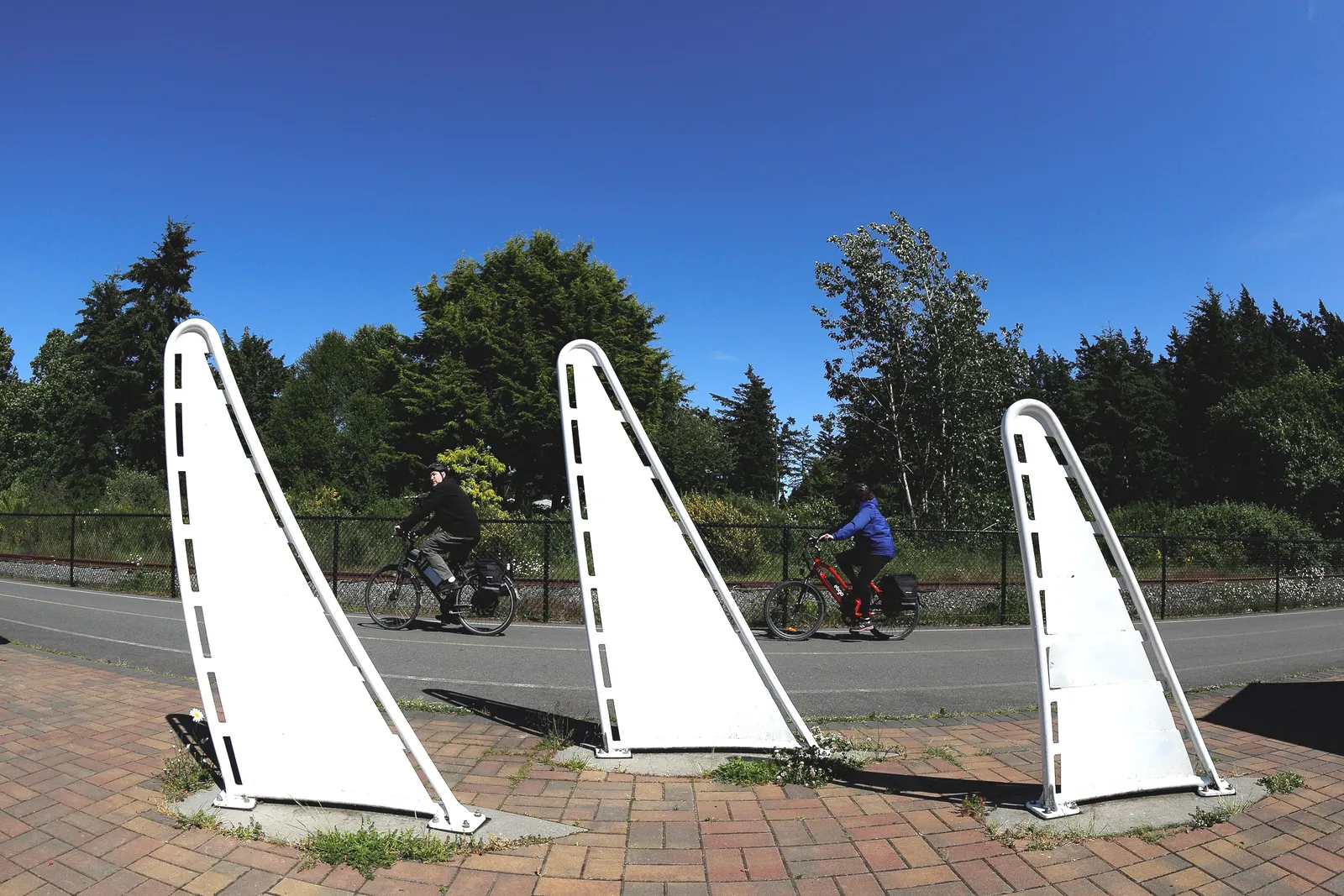 Public art sculptures shaped like sails next to a paved path with cyclists