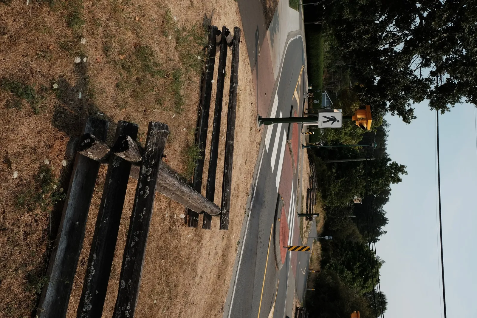 A pedestrian crossing sign and rustic wooden fence along a road