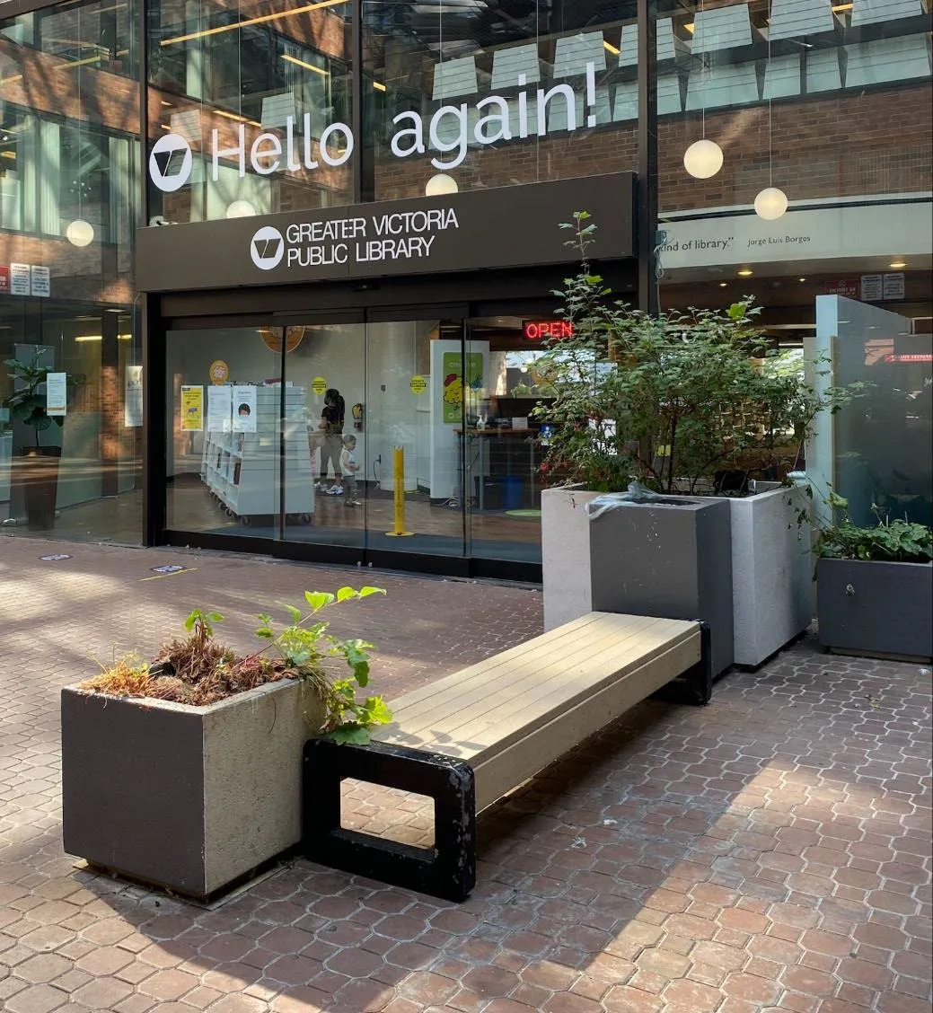 Entrance of a Greater Victoria Public Library branch with a bench and planters in front.