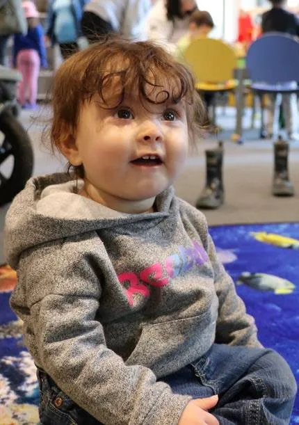 Close-up photo of a young child smiling while sitting on a colorful carpet.